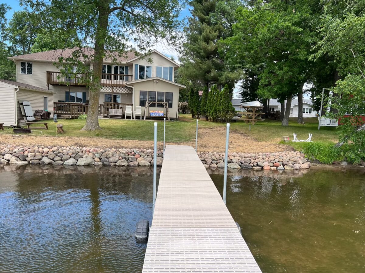 Rock shoreline installation with dock, lake house in background